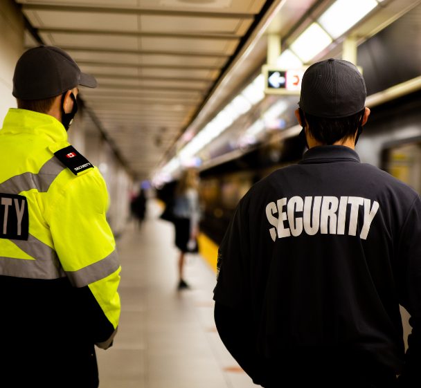 Two security officers, one in hi-vis, in a station concourse